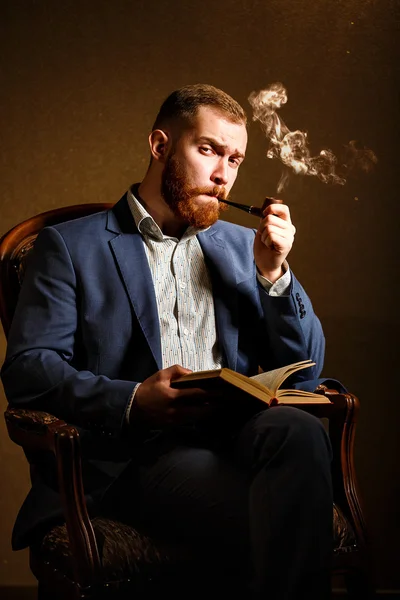 Retrato de un joven guapo en traje azul fumando una pipa y leyendo un libro — Foto de Stock