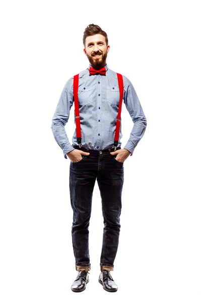 Stylischer Typ mit blauem Hemd, roter Fliege und Hosenträgern in Weiß. Lächeln. stehen. Hände in der Tasche. — Stockfoto