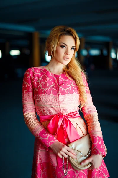 Fashion photo of beautiful young girl with blond hair wearing luxurious pink dress, bag at underground parking. — Stock Photo, Image