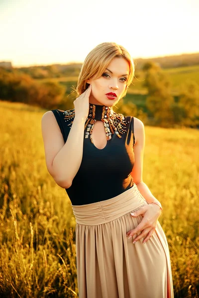 Foto de moda de menina bonita com cabelo loiro vestindo vestido bege luxuoso no pôr do sol . — Fotografia de Stock