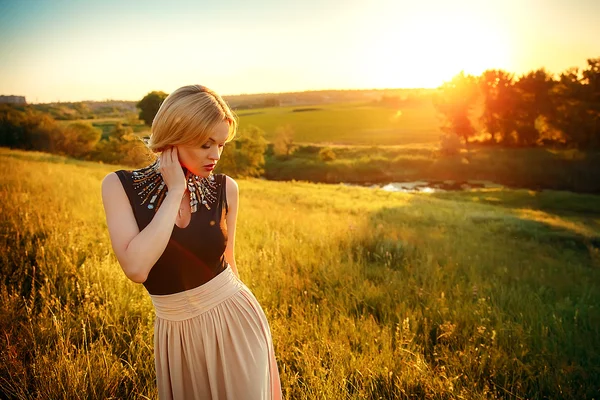 Foto de moda de menina bonita com cabelo loiro vestindo vestido bege luxuoso no pôr do sol . — Fotografia de Stock