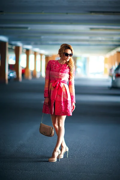 A szép, fiatal lány, szőke hajat visel luxus rózsaszín ruha, táska: mélygarázs divatfotózás. — Stock Fotó
