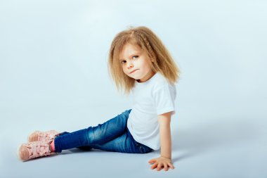 little girl 4 years old with curly hair wearing white shirt, blue jeans, pink boots sitting on the floor, smiling and looking at camera.