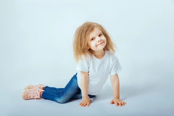 Little girl 4 years old with curly hair wearing white shirt, blue jeans, pink boots sitting on the floor, smiling and looking at camera. — 스톡 사진