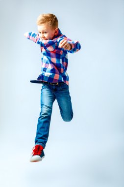 Jumping little boy in the colorful plaid shirt, blue jeans, gumshoes. Isolated.