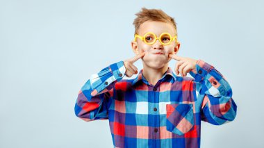 Little boy wearing colorful plaid shirt, plastic glasses having fun in the studio clipart