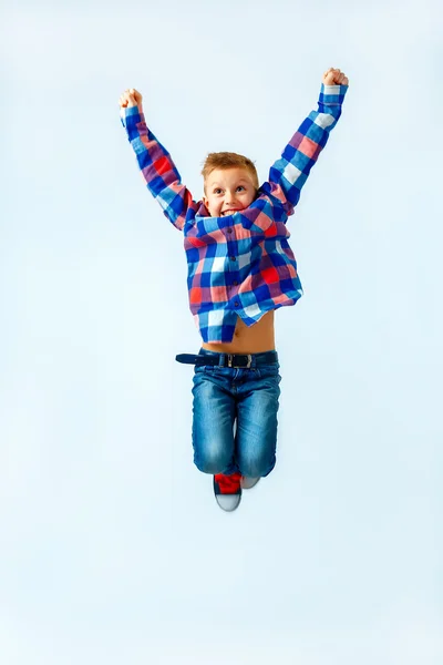 Jumping little boy in the colorful plaid shirt, blue jeans, gumshoes. Isolated. — Stock Fotó