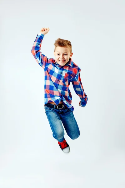 Jumping little boy in the colorful plaid shirt, blue jeans, gumshoes. Isolated. — Stock Fotó