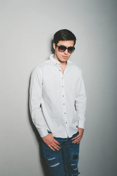 Young man in shorts and white shirt is smiling standing near the wall with glasses — Stock Photo, Image