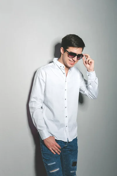 Νεαρός άνδρας με σορτς και λευκό πουκάμισο χαμογελάει στέκεται κοντά στον τοίχο με γυαλιά — Φωτογραφία Αρχείου