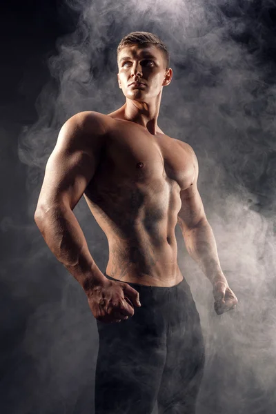 Bellissimo potere atletico uomo bodybuilder. Fitness corpo muscolare su sfondo scuro fumo. Maschio perfetto. bodybuilder impressionante, tatuaggio, posa . — Foto Stock