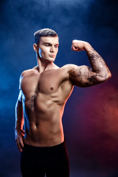 Beau bodybuilder homme athlétique de puissance. Fitness corps musclé sur fond de fumée sombre. Homme parfait. bodybuilder génial, tatouage, posant . — Photo