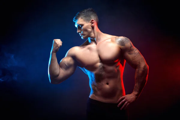 Bellissimo potere atletico uomo bodybuilder. Fitness corpo muscolare su sfondo scuro fumo. Maschio perfetto. bodybuilder impressionante, tatuaggio, posa . — Foto Stock