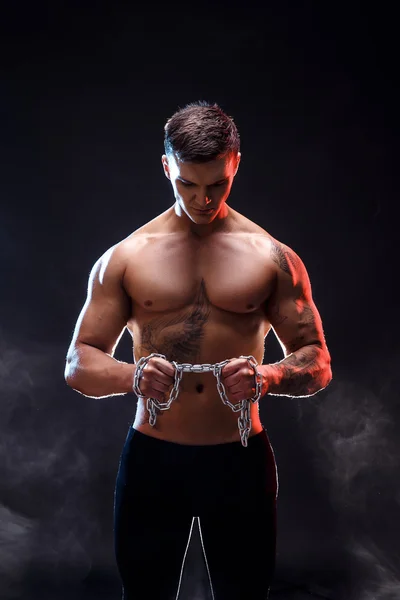 Gros plan d'un beau bodybuilder d'homme athlétique de puissance faisant des exercices avec la chaîne. Fitness corps musculaire sur fond sombre. Homme parfait. bodybuilder génial, tatouage, posant . — Photo