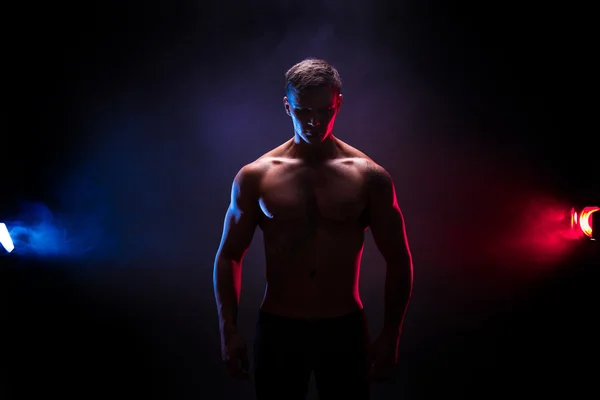 Sziluettjét félelmetes testépítő. Szép teljesítmény sportos férfi testépítő. Fitness izmos test, füst, sötét színű háttérben. Tökéletes férfi. tetoválás, pózol. — Stock Fotó