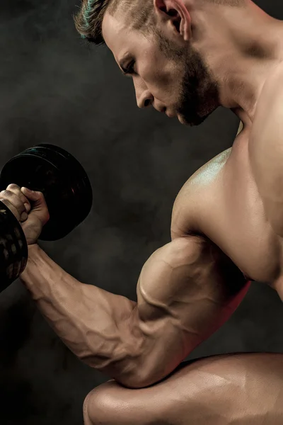 Closeup bir yakışıklı güç atletik erkek vücut dumbbell ile yapıyor. Fitness kas vücut koyu arka plan üzerinde. Seçici odak. Harika vücut geliştirmeci, poz. — Stok fotoğraf