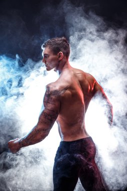 Yakışıklı güç atletik erkek vücut geliştiricisi. Fitness kas vücut koyu duman arka plan üzerinde. Mükemmel erkek. Harika vücut geliştirmeci, dövme, poz.