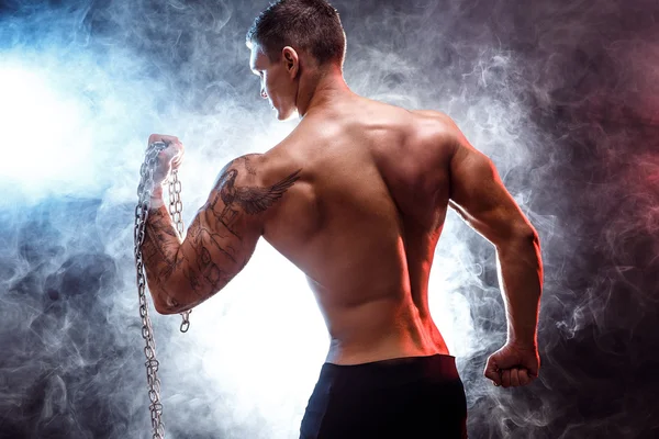 Primer plano de un atractivo poder atlético hombre culturista haciendo ejercicios con cadena. Cuerpo muscular fitness sobre fondo oscuro. Hombre perfecto. Culturista impresionante, tatuaje, posando . — Foto de Stock