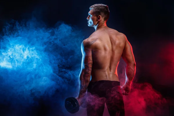 Stand halterle dinlenme bir yakışıklı güç atletik erkek vücut geliştirmeci closeup. Fitness kas vücut koyu duman arka plan üzerinde. Mükemmel erkek. Harika vücut geliştirmeci, dövme, poz.