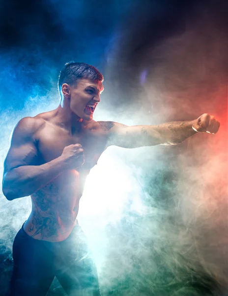 Combatiente muscular golpeando en el humo. Fondo de color . — Foto de Stock