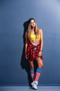 Sihir seksi güzel genç kadın modeli spor gömlek, şapka, kırmızı, kırmızı kelepçe izle, beyaz spor ayakkabı, tozluk ile ABD bayrağı, gülümseyen dokulu duvara yaslandı