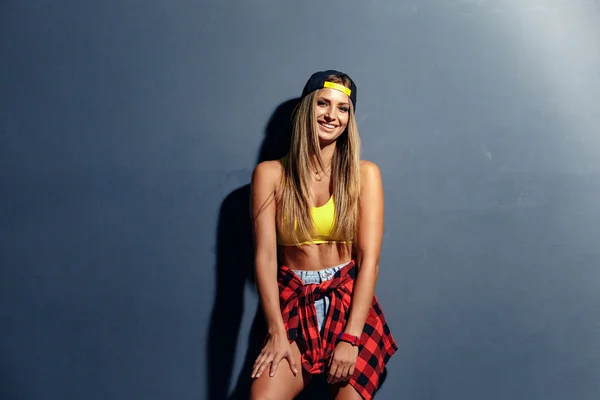 Muchacha muy joven de moda con una gorra y camisa a cuadros en el estudio, apoyado en la pared texturizada. Sonríe boca abierta con dientes blancos perfectos —  Fotos de Stock