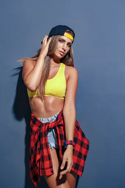 Fashion pretty young girl wearing a cap and checkered shirt in studio, leaned on textured wall — Stock Photo, Image