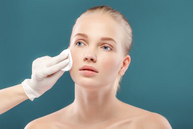 Mükemmel cilt ile genç güzel kadın portre portre. Temiz sünger uygulanıyor. Onun yüzünü yıkama. Mavi izole.