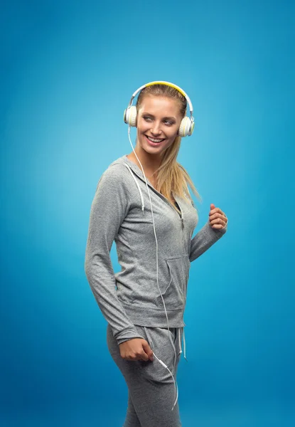 金发美女适合白种人女士灰色运动中戴着耳机听音乐。蓝色背景上孤立. — 图库照片
