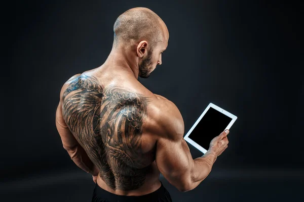 Без рубашки лысый татуированный человек с помощью планшета стоять в стороне — стоковое фото
