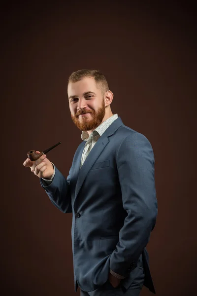 Elegante hombre sonriente con barba sosteniendo pipa humeante — Foto de Stock