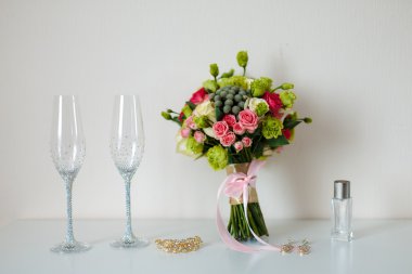 Gelin güzel romantik buket çeşitli çiçekler, şampanya, parlak taşlar, altın bir saç tokası, küpe için gözlük. Seçici odak.