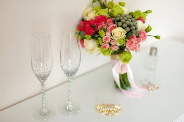 Bridal beautiful romantic bouquet of various flowers, glasses for champagne, in brilliant stones, a gold hairpin, earrings. Selective focus. — Stock Photo, Image