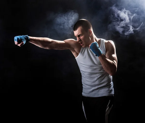 Svalnatý kickbox nebo muay thai bojovník děrování v kouři. — Stock fotografie