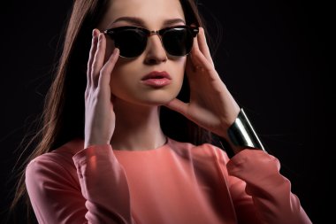 Güneş gözlüklü genç bir kadın kameraya bakıyor.