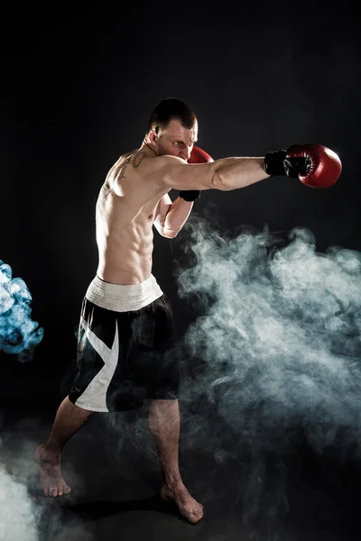 Muscular kickbox o muay thai luchador puñetazos en el humo . —  Fotos de Stock