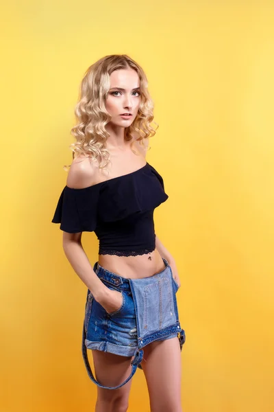 Vacker blond modell med lockigt hår poserar på kameran på gula studio bakgrund — Stockfoto