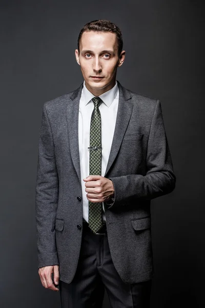 Серьезный бизнесмен каштановые волосы с выразительным лицом в сером костюме и галстуке. Изолированный на тёмном фоне . — стоковое фото