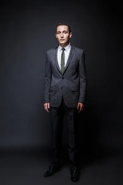 Homem de negócios sério cabelo castanho com rosto expressivo vestindo terno cinza e gravata. Isolado em fundo escuro . — Fotografia de Stock