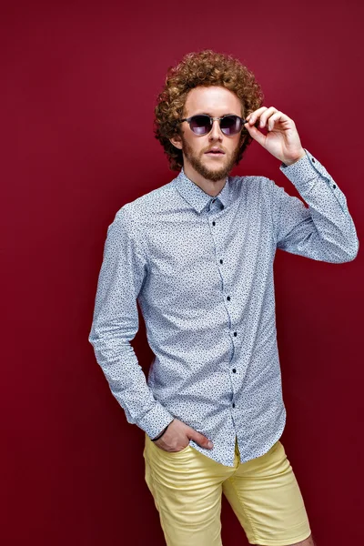 Elegante hombre de pelo rizado en gafas de sol sobre fondo rojo — Foto de Stock