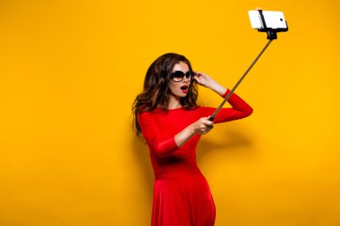 Harika elbise ve kırmızı güzel esmer portresi giyen güneş gözlüğü selfie sopa ile yaparken dudakları. İzole