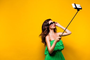 Yeşil elbise ve selfie sarı arka plan yaparken poz güneş gözlüğü genç model portresi.
