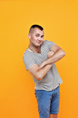 Çizgili bir gömlek ve mavi şort gülümseyen adam kollar göğüs üzerinde geçti. Parlak, sarı arka plan