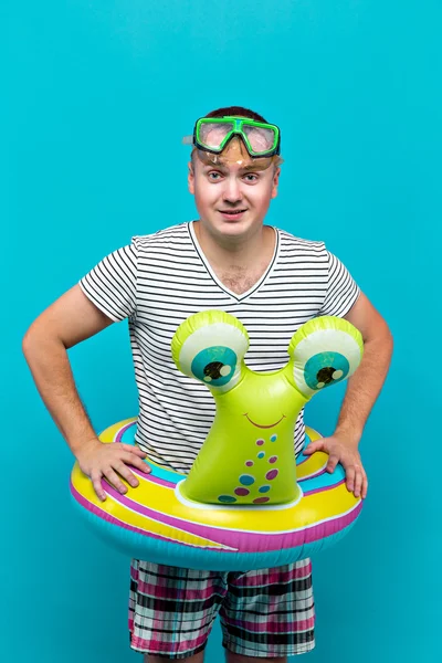 Hombre con una máscara submarina, camisa a rayas, vueltas de baño en forma de un caracol mirando a la cámara, fondo azul. Concepto de vacaciones —  Fotos de Stock