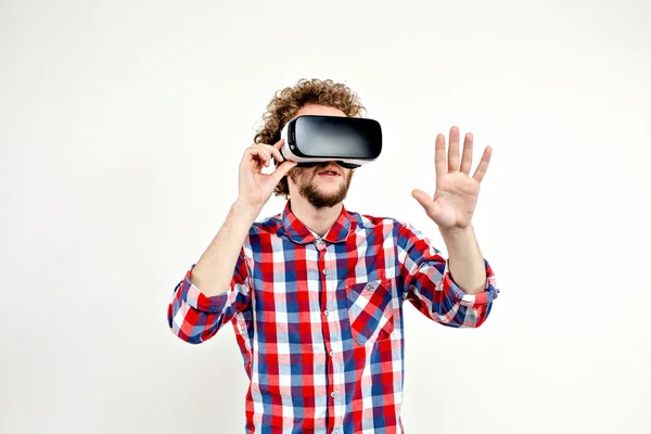 Joven hombre de pelo rizado con camisa a cuadros usando un auricular VR y experimentando realidad virtual aislado sobre fondo blanco — Foto de Stock