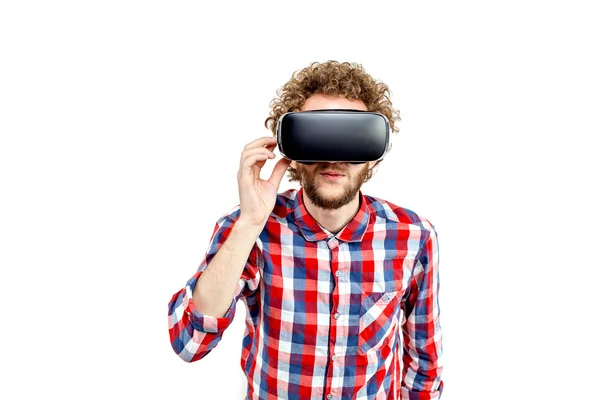 Joven hombre de pelo rizado con camisa a cuadros usando un auricular VR y experimentando realidad virtual aislado sobre fondo blanco — Foto de Stock