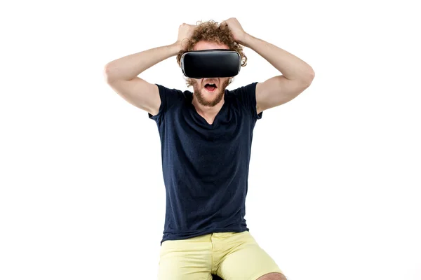 Молодий кучерявий чоловік використовує гарнітуру VR і відчуває віртуальну реальність ізольовано на білому тлі — стокове фото
