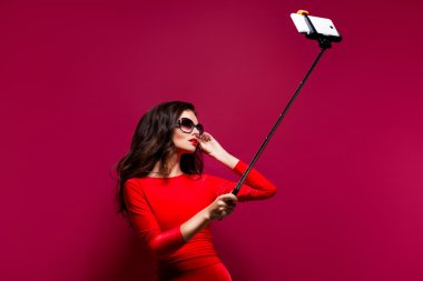Harika elbise ve kırmızı güzel esmer portresi giyen güneş gözlüğü selfie sopa ile yaparken dudakları. İzole
