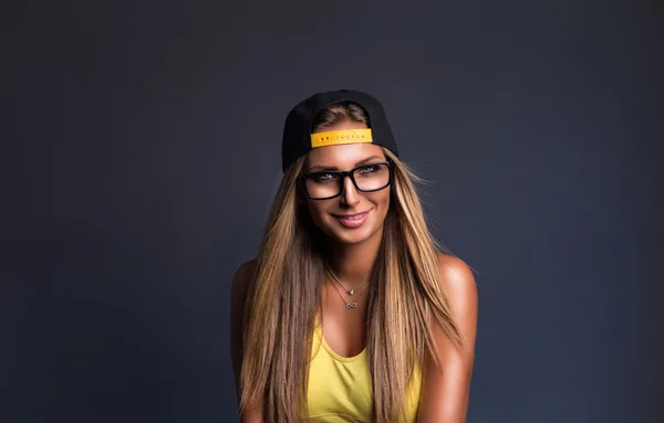 Hermosa chica en gorra y gafas sentado en la silla, fondo gris —  Fotos de Stock