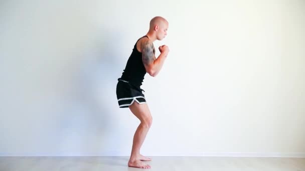 Un jeune homme en forme faisant des squats avec une cloche de bouilloire dans une petite salle de gym — Video